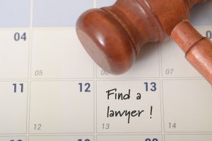 A gavel placed next to a calendar with a handwritten note reading "Find a lawyer!", highlighting a pressing need for legal assistance.