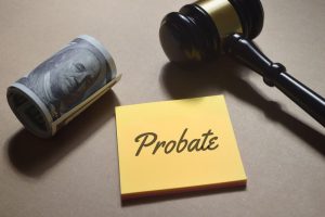 Top view of a judge's gavel and scattered money next to the word 'Probate' on a wooden surface.