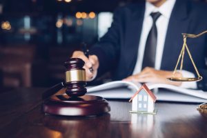 Real estate law concept showing a male judge holding a gavel over a sounding block at a desk, reviewing case documents in a modern office.