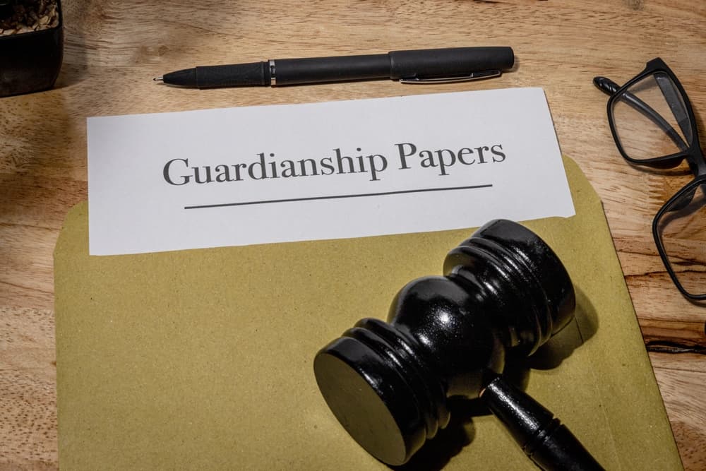 Guardianship legal document partially pulled from an envelope, lying next to a judge’s gavel on a wooden surface.