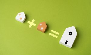 Concept image showing two smaller houses being exchanged for one large modern home, symbolizing spouses selling individual properties to buy joint real estate with mortgages or loans.