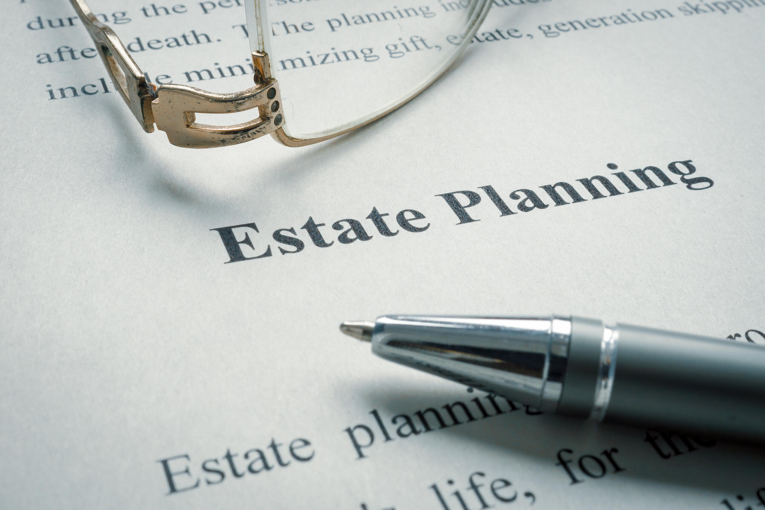 A close-up view of a printed document featuring the words "Estate Planning" in large text, positioned next to a silver pen and a pair of gold-rimmed eyeglasses, representing documentation relevant to Florida executor disputes: what you need to know.
