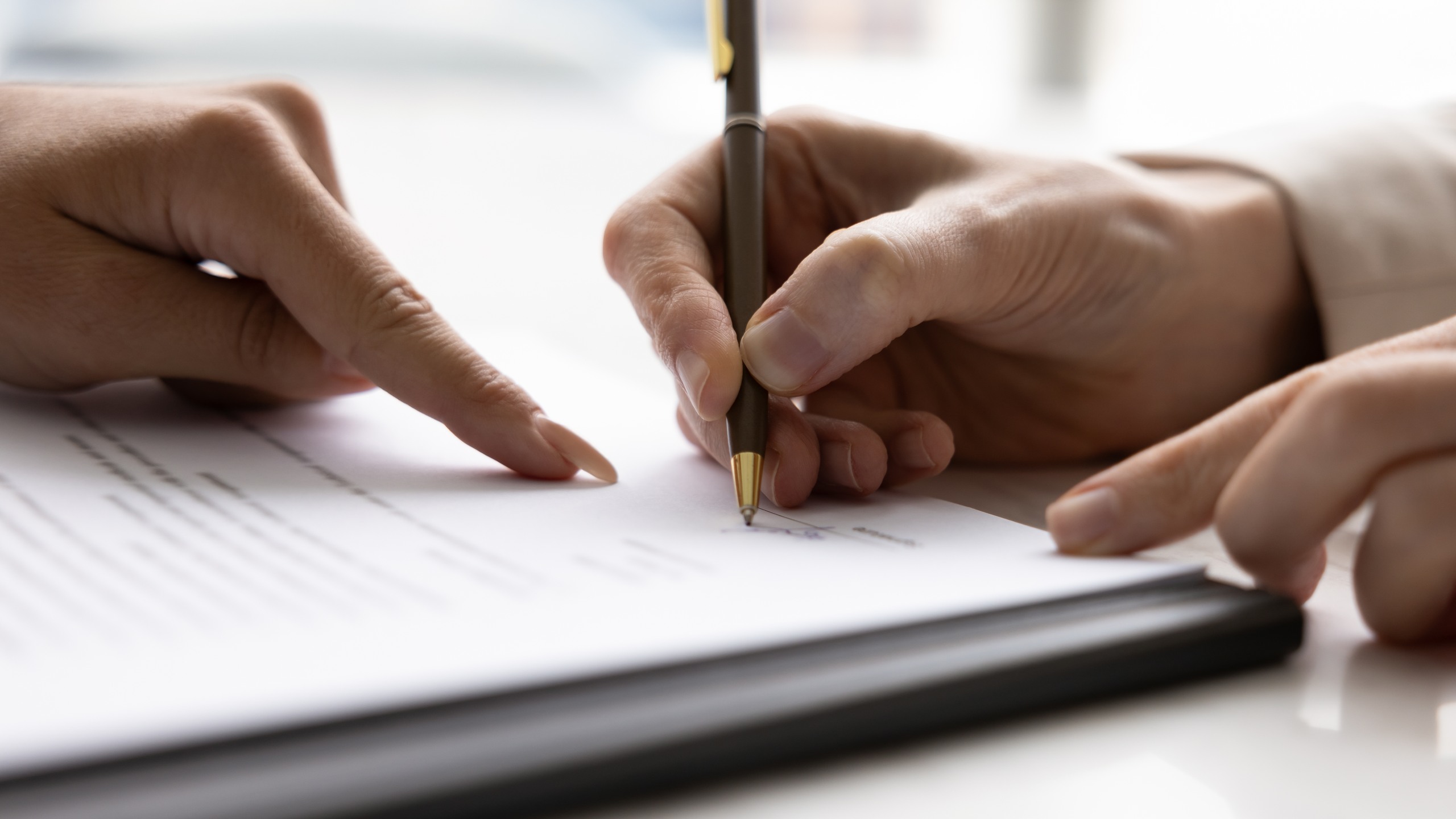 A close-up view of one person's hand holding a pen to sign a document while another person points directly at the signature line, illustrating the pressure tactics examined when asking what is undue influence in a Florida will.